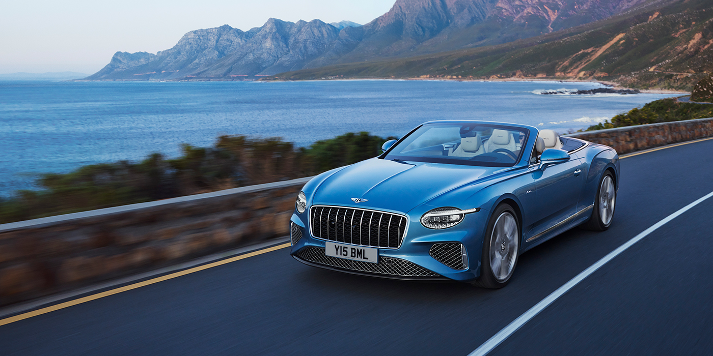 Bentley Barcelona New Bentley Continental GTC Azure convertible in Light Windsor blue paint with 22 inch Azure wheels and chrome grill, driving dynamically by the sea