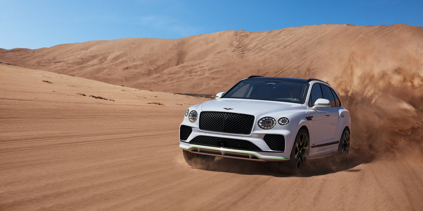 Bentley Barcelona Bentley Bentayga Speed SUV front three quarter in Snow Quarts Pearlescent by Mulliner white paint driving dynamically through the desert