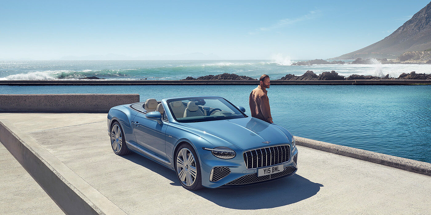 Bentley Barcelona New Bentley Continental GTC Azure convertible front view in Light Windsor blue paint with 22 inch ten spoke wheels parked by the sea in the sunshine