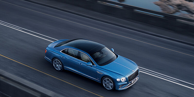 Bentley Barcelona New Bentley Flying Spur Azure sedan in Light windsor blue paint by Mulliner, with 22 inch Azure wheels seen from overhead driving dynamically on a country road