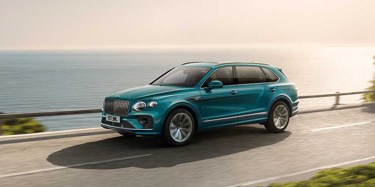 Bentley Barcelona Bentley Bentayga Extended Wheelbase Azure SUV in Topaz blue paint driving dynamically by the ocean