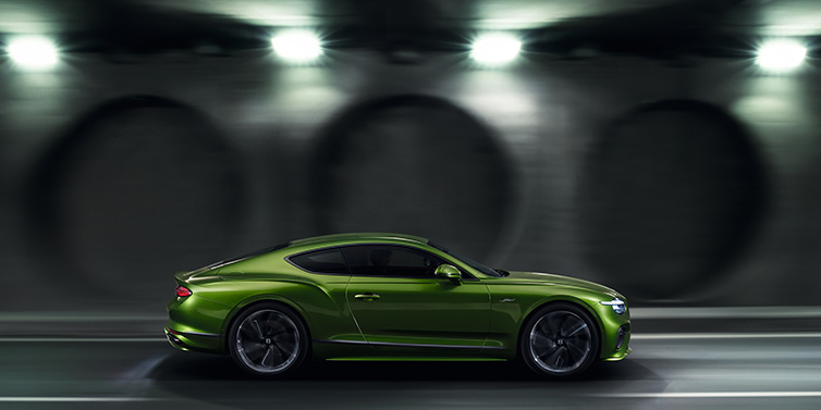 Bentley Barcelona Bentley Continental GT Speed coupe profile in Tourmaline Green driving dynamically past a concrete wall at night