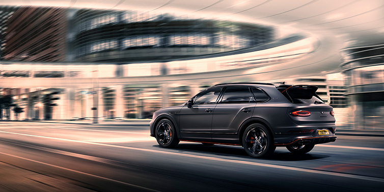 Bentley Barcelona Bentley Bentayga S Black Edition SUV rear three quarter in Anthracite Satin paint driving dynamically through a city at night