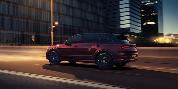 Bentley Barcelona Bentley Bentayga Extended Wheelbase Mulliner SUV in Cricket Ball red paint driving dynamically in city at night