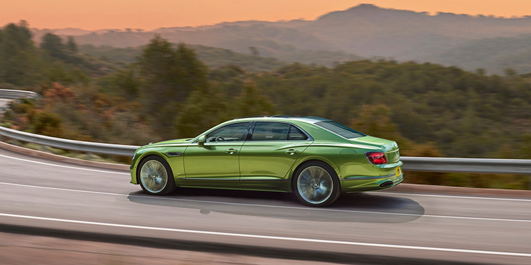 Bentley Barcelona Bentley Flying Spur Speed sedan side profile in Tourmaline Green paint driving dynamically on a mountain road at sunset