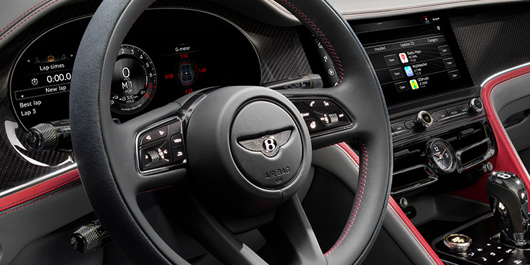 Bentley Barcelona Bentley Flying Spur Speed sedan front interior detail showing steering wheel and driver screens surrounded with Hotspur red and Gravity Grey hides